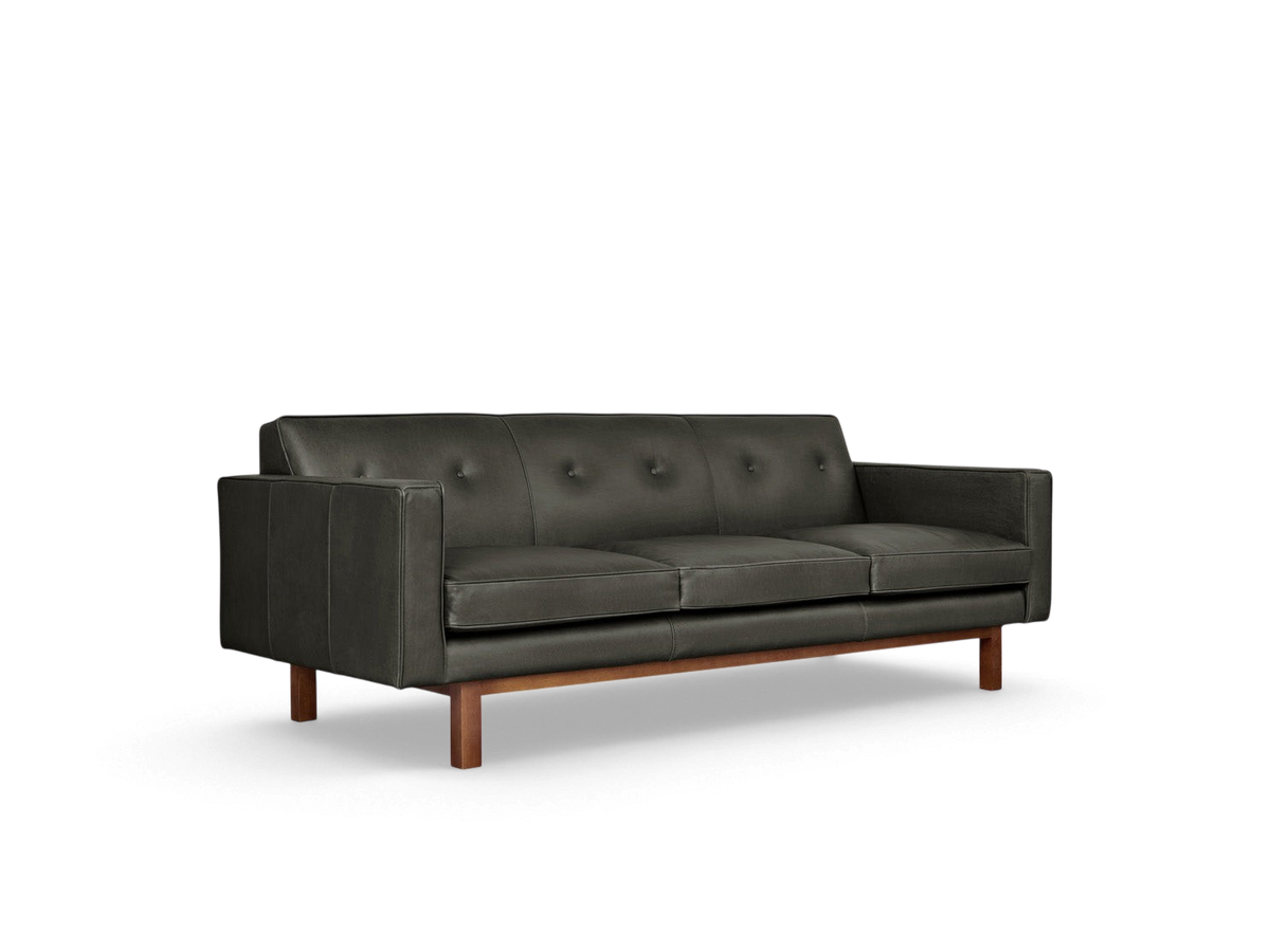 urbane EQ3 Embassy Sofa in dark leather with button-tufted back, piping details, and a walnut-stained wood base.